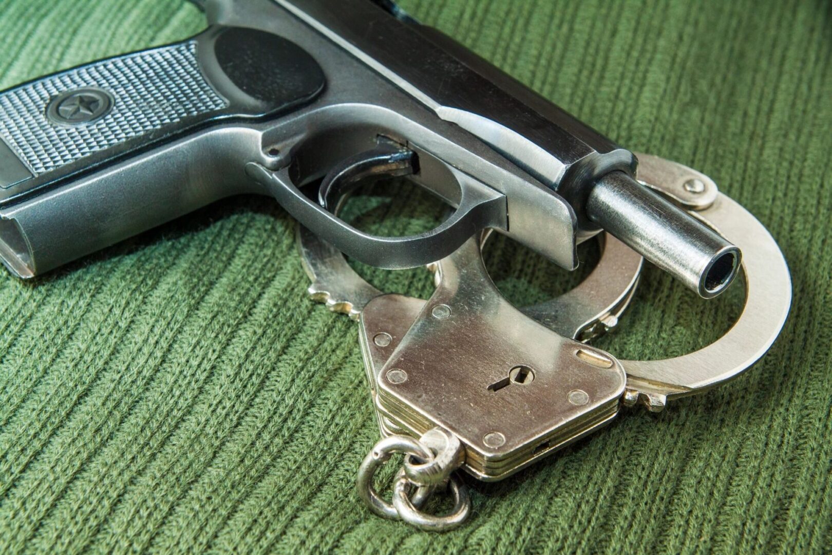 A gun and handcuffs on top of a green cloth.